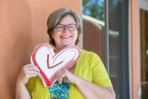 Karen Delaney, Executive Director, smiles brightly while holding the heart of the Volunteer Center logo.