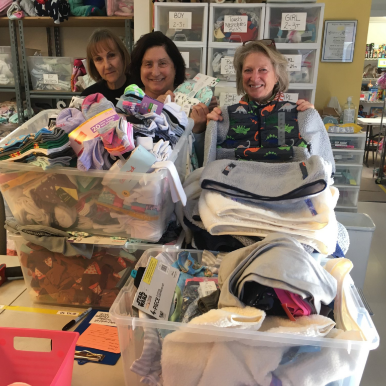 Volunteers stand with bins of clothes and supplies for children in need